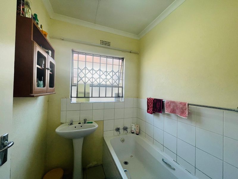 A functional bathroom featuring a pedestal basin, bathtub, and tiled splashback, requiring cosmetic updates to modernize the space.