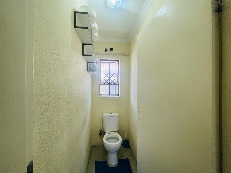 A compact, functional bathroom featuring a standard toilet, security-barred window, and built-in wall shelving.