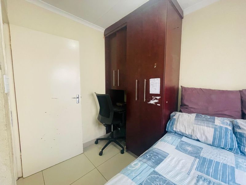 A functional bedroom featuring tiled flooring, coving, and a built-in wardrobe with an integrated desk space.