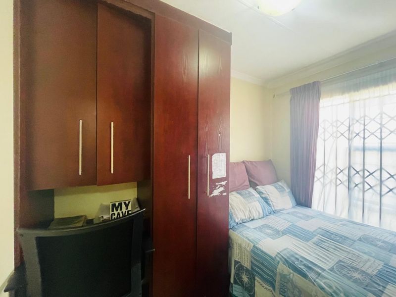 A bedroom featuring a built-in wardrobe with integrated desk space and a window fitted with a security gate.