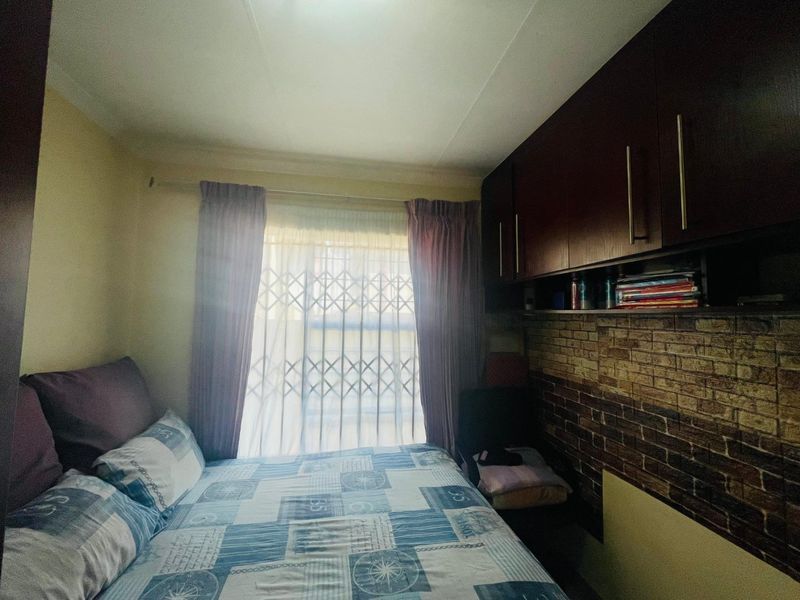 A bedroom featuring built-in dark wood cabinetry, a brick-effect feature wall, and a window fitted with a security gate.