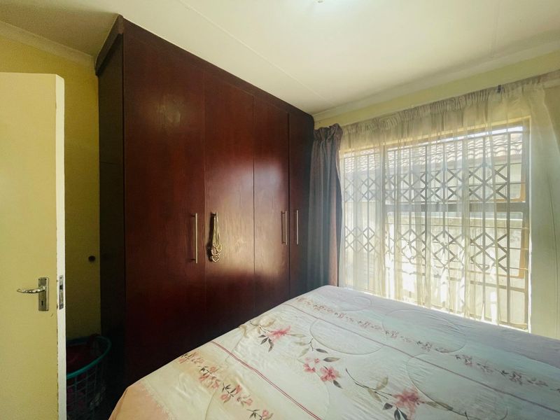 A bedroom featuring a large built-in wooden wardrobe and a window fitted with a security gate.