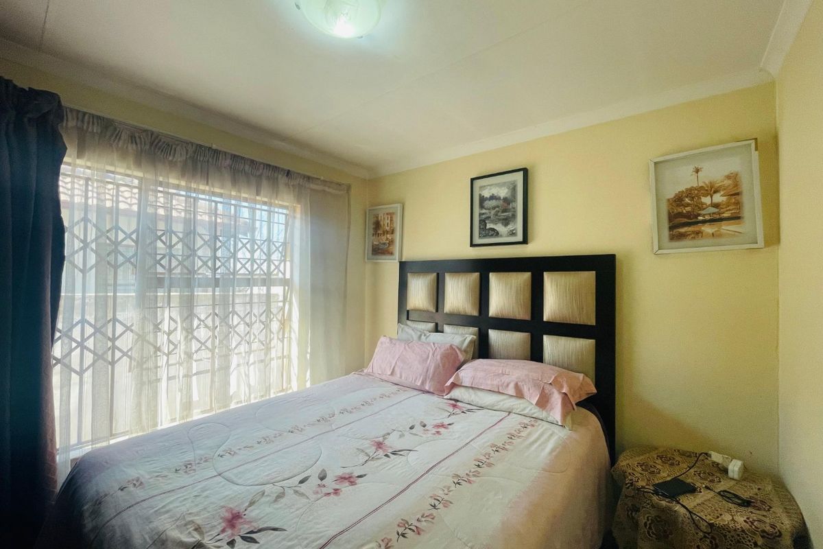A standard bedroom featuring a coved ceiling, central light fixture, and a window fitted with a security gate.