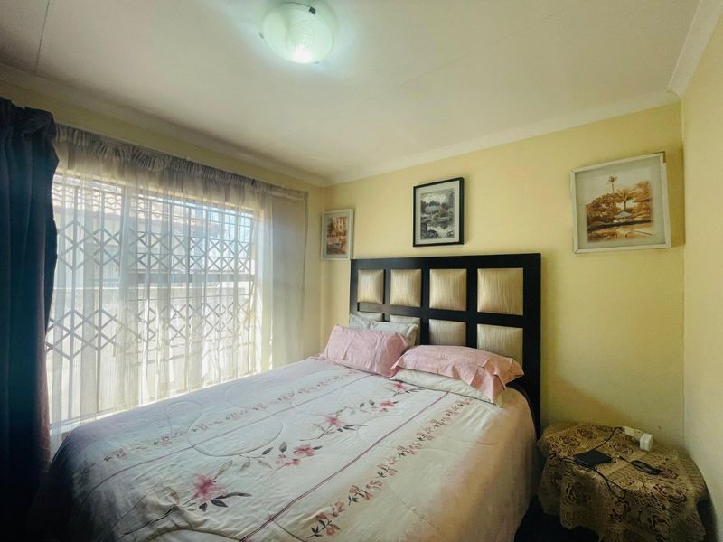 A standard bedroom featuring a coved ceiling, central light fixture, and a window fitted with a security gate.