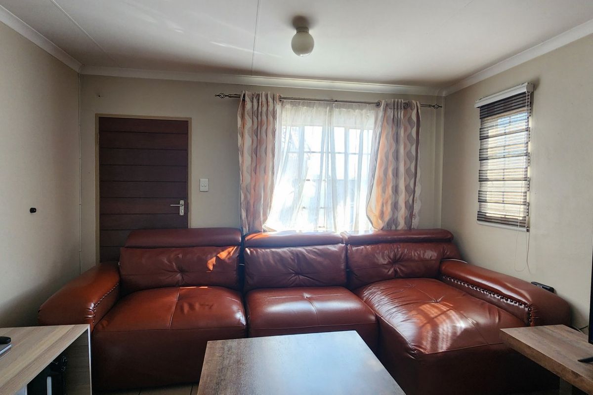 A comfortable living room featuring neutral walls, cove cornicing, and natural light through a window with fitted blinds and curtains.