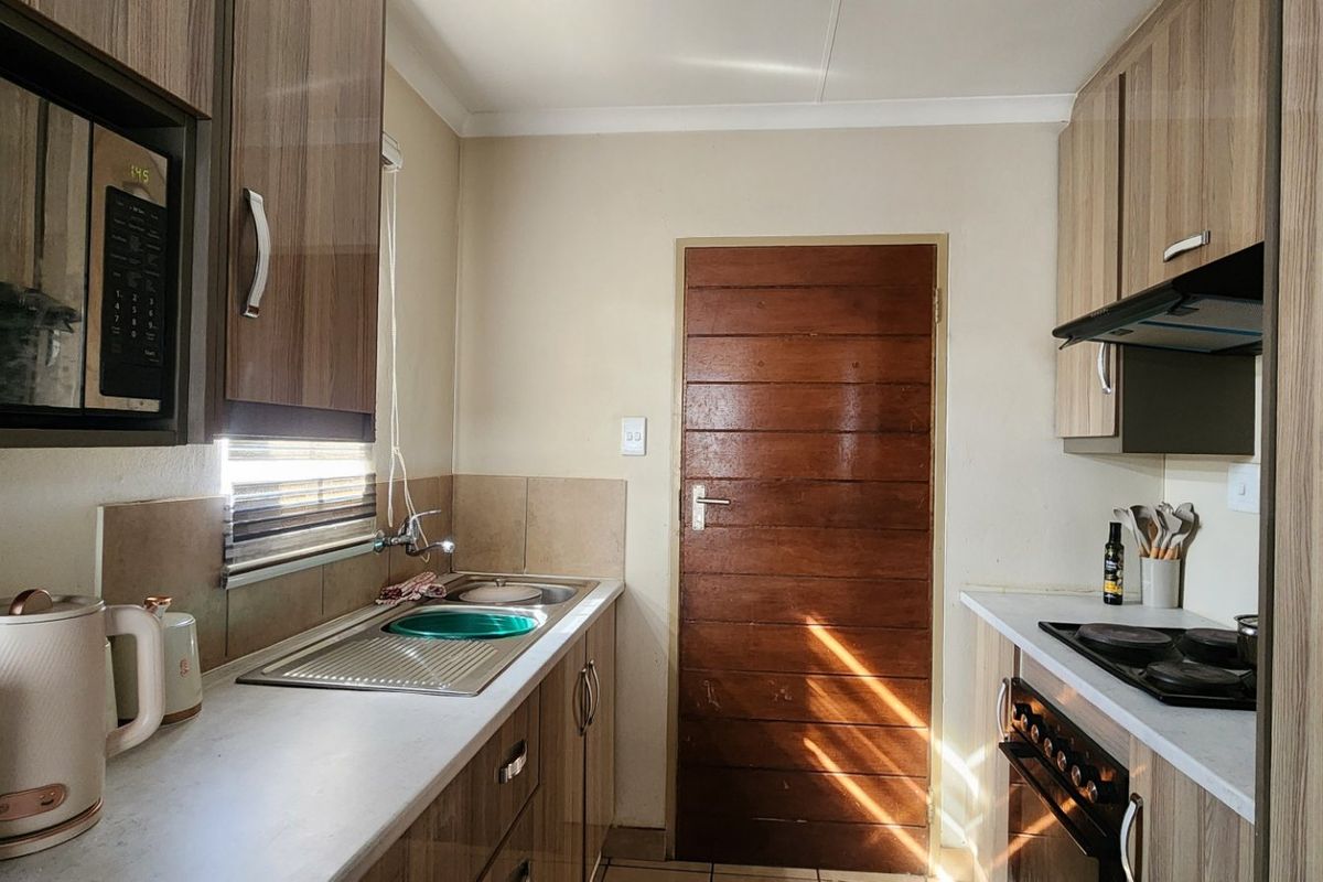 A functional galley-style kitchen featuring wood-look laminate cabinetry, a stainless steel sink, built-in oven, and electric hob with an extractor fan.