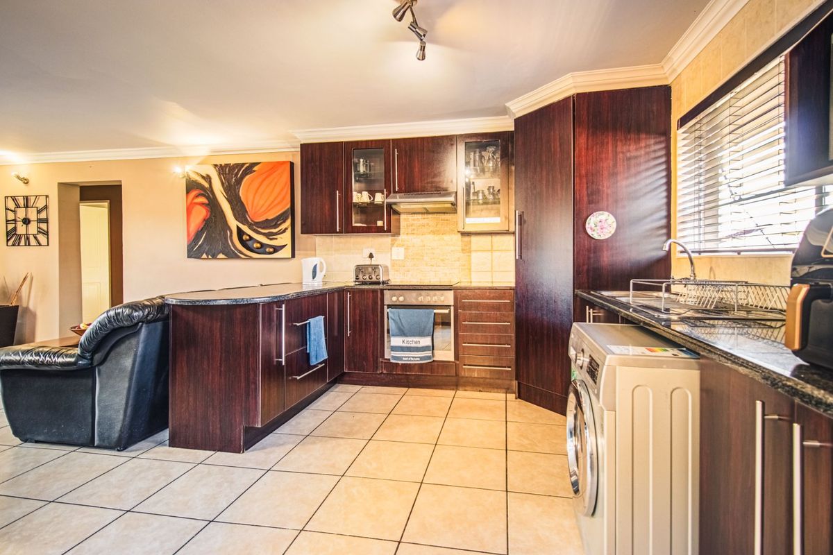 A functional kitchen featuring dark wood cabinetry, granite countertops, built-in oven, extractor fan, and tiled flooring, integrated into an open-plan living space.