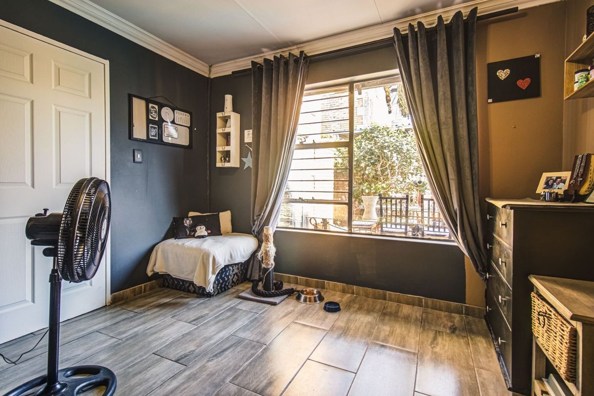 A bedroom featuring wood-look tiled flooring, crown molding, and a large window with security bars, offering natural light and garden views.