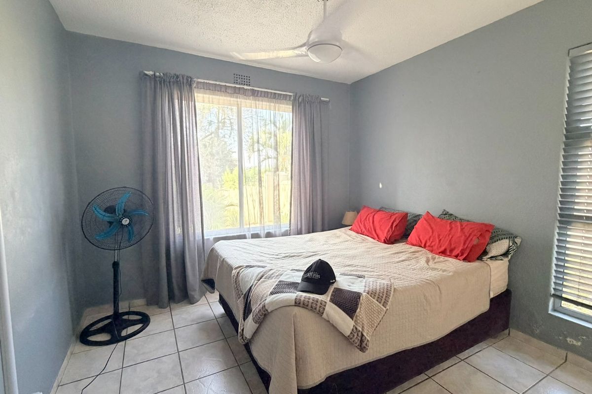 A bedroom featuring tiled flooring, a ceiling fan, and dual window treatments, providing a functional space with potential for cosmetic updates.