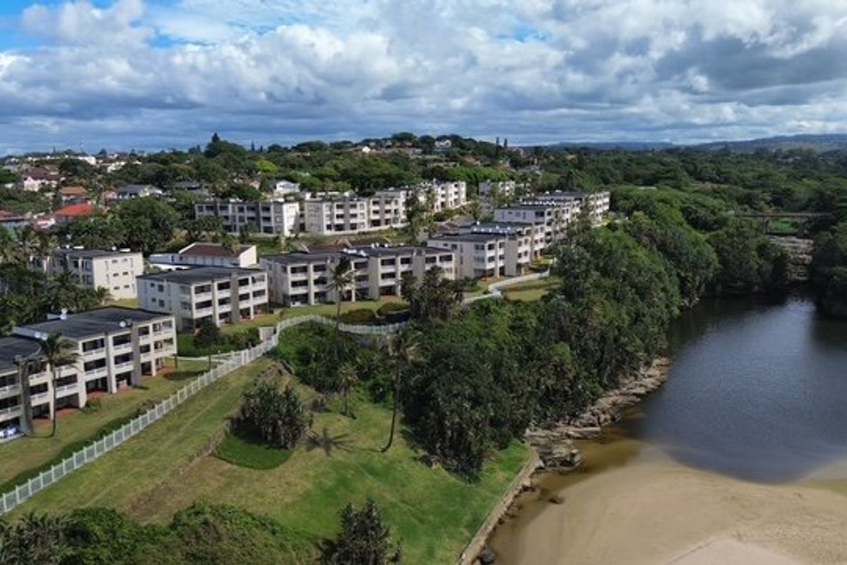 Aerial view of a multi-story apartment complex situated along a riverfront, featuring landscaped grounds and secure perimeter fencing.