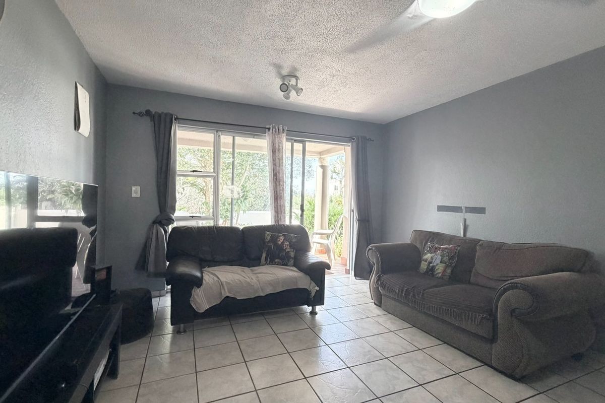 A living room featuring ceramic floor tiles, a textured ceiling, and sliding glass doors providing access to an outdoor patio area.