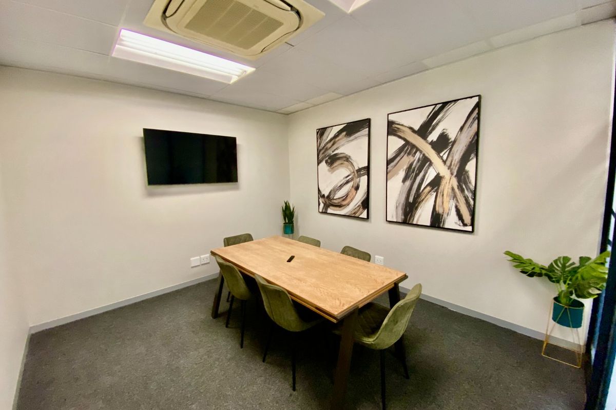 A professional office meeting room featuring carpeted flooring, recessed ceiling air conditioning, and a wall-mounted television.