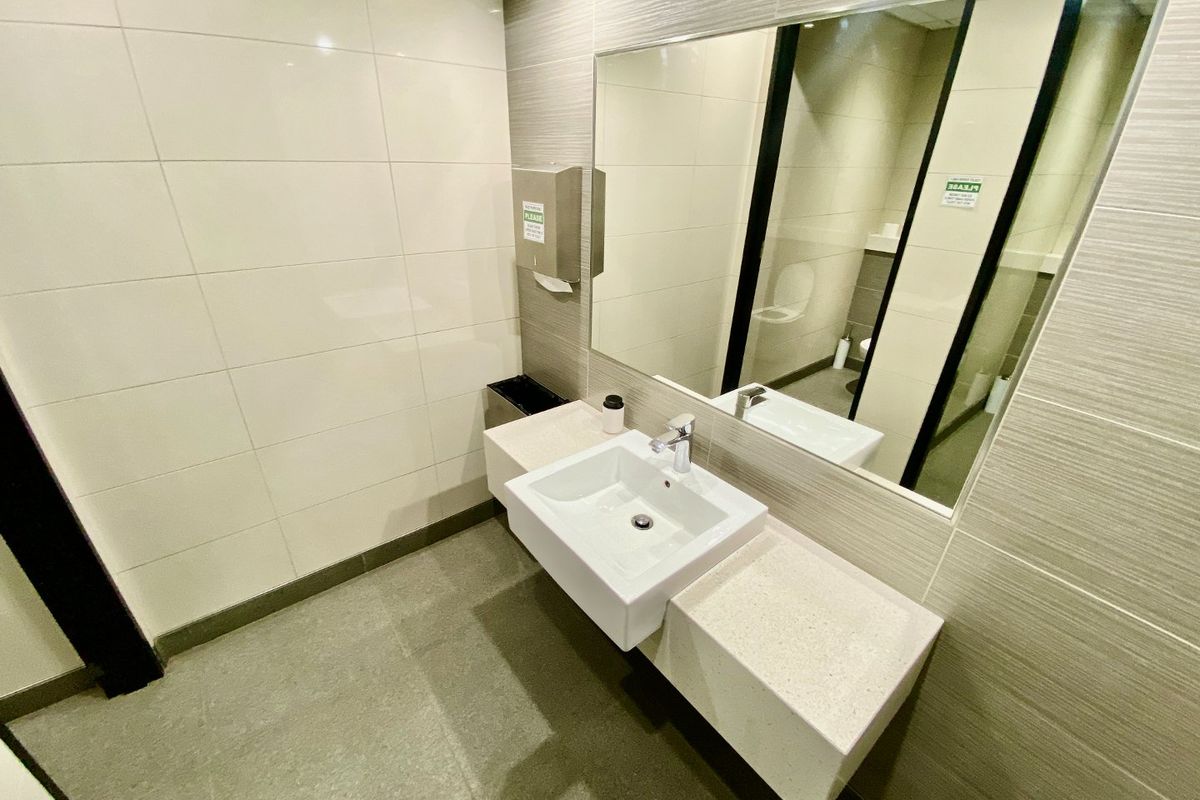A clean, modern commercial bathroom featuring a wall-mounted vanity with a ceramic basin, chrome mixer tap, and a large integrated wall mirror.