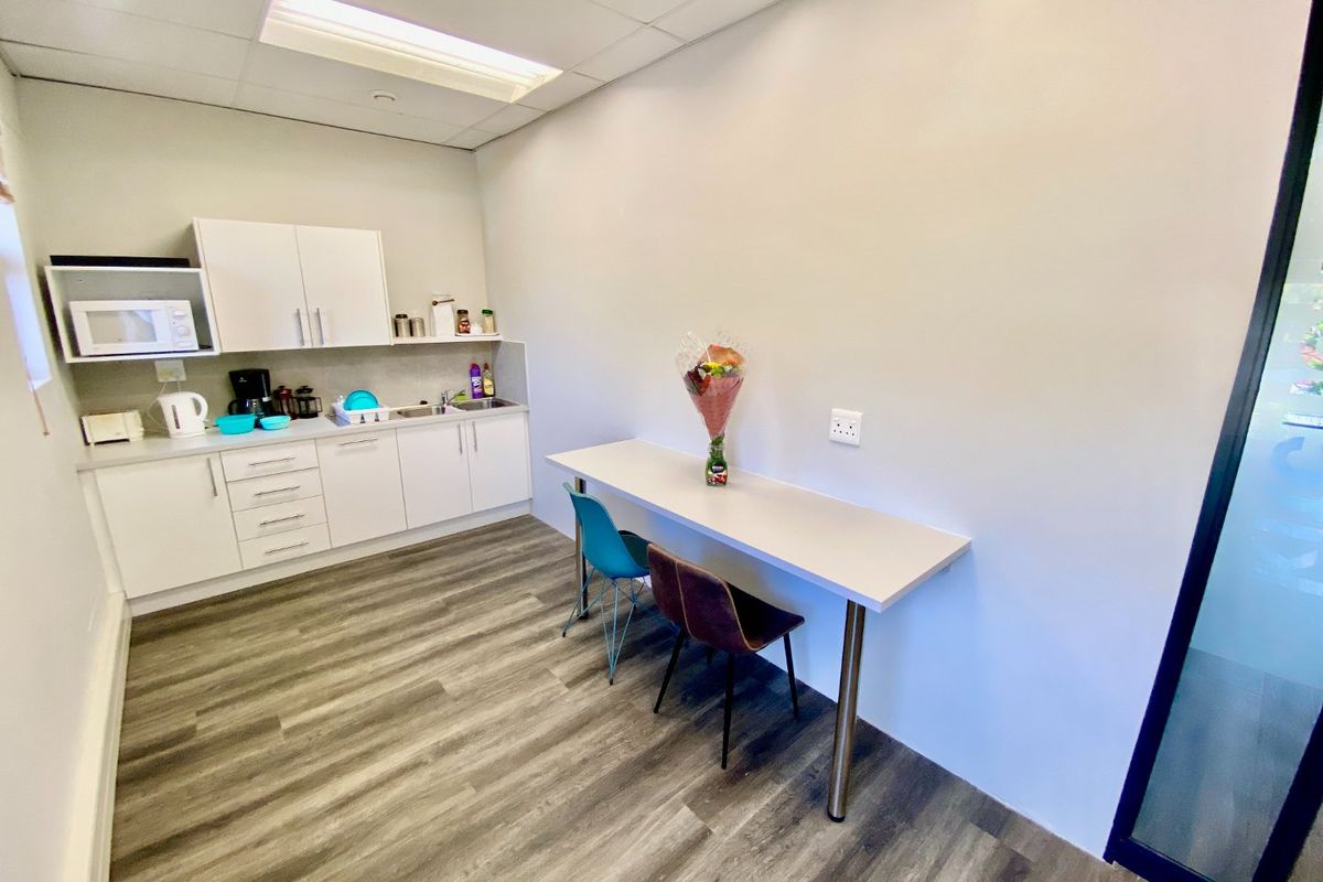 A clean, modern commercial kitchenette featuring white cabinetry, wood-look laminate flooring, and a wall-mounted breakfast bar.