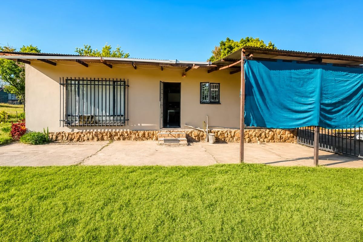 Rear view of the property featuring a concrete patio, stone cladding base, security bars on windows, and a corrugated metal roof structure.