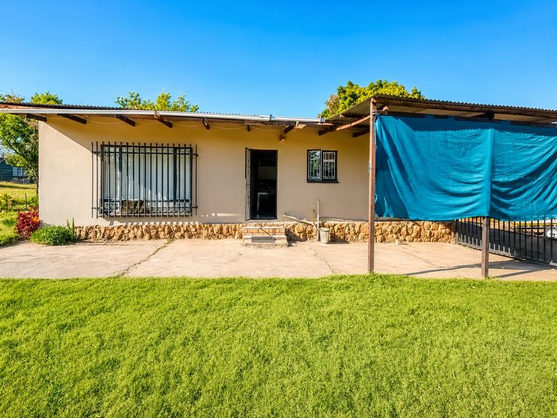 Rear view of the property featuring a concrete patio, stone cladding base, security bars on windows, and a corrugated metal roof structure.