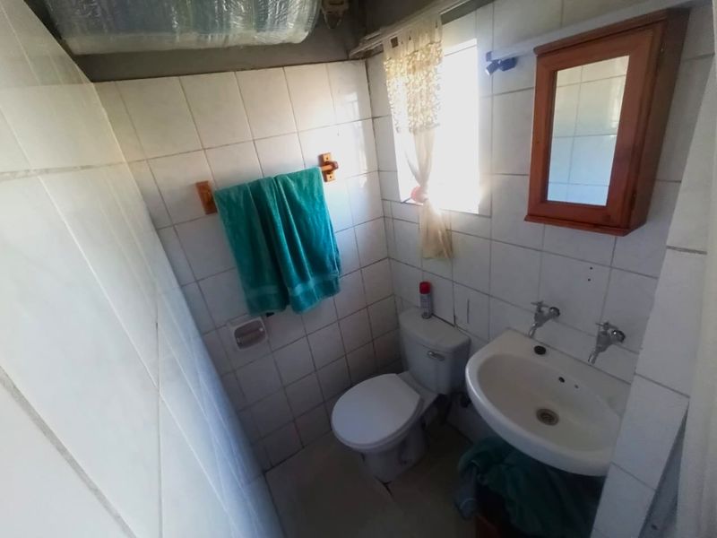 A compact bathroom featuring a pedestal basin, toilet, and wall-mounted medicine cabinet, requiring cosmetic updates to the tiling and ceiling finishes.