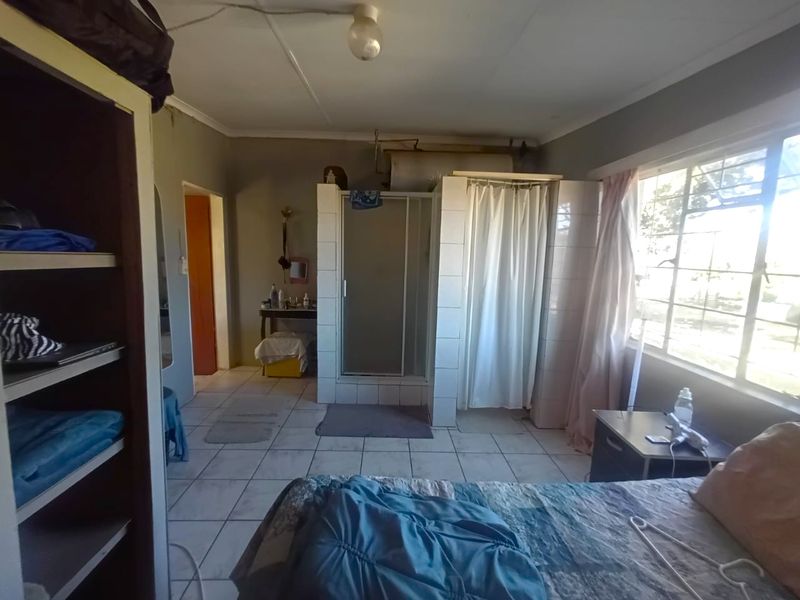 Bedroom featuring an integrated shower cubicle, tiled flooring, and large windows. The space requires modernization of the shower area and ceiling finishes.