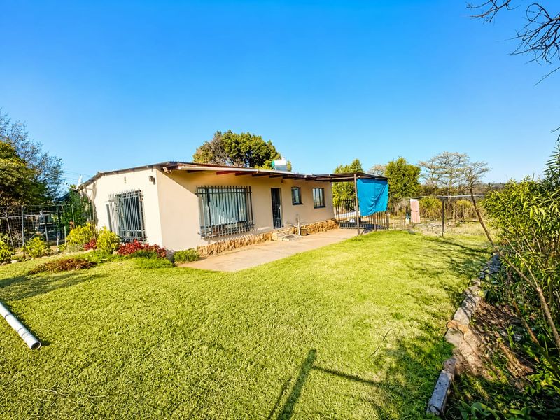 Rear view of the property featuring a covered patio, security bars on windows, and a spacious garden area with stone cladding base details.