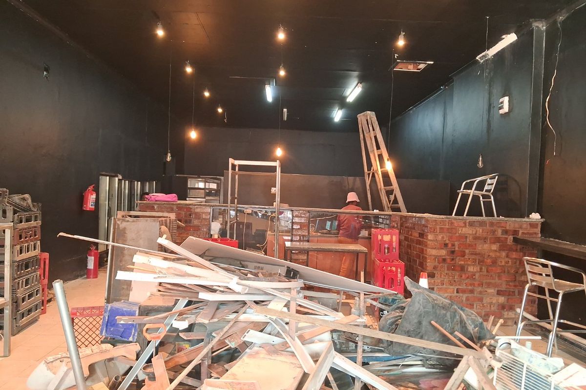 Open plan commercial space featuring an exposed brick counter and dark painted walls, currently undergoing renovation with significant debris present.