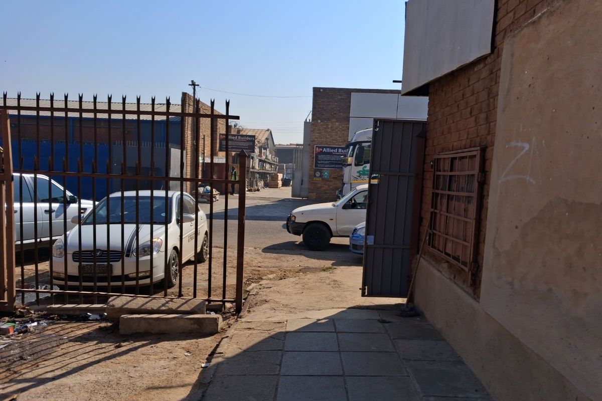 Exterior view of a commercial property entrance featuring metal security fencing, a paved walkway, and brick building facade.