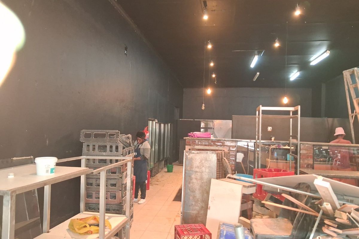 Commercial kitchen space featuring tiled flooring, exposed ceiling with pendant lighting, and a brick service counter, currently in need of organization and refurbishment.
