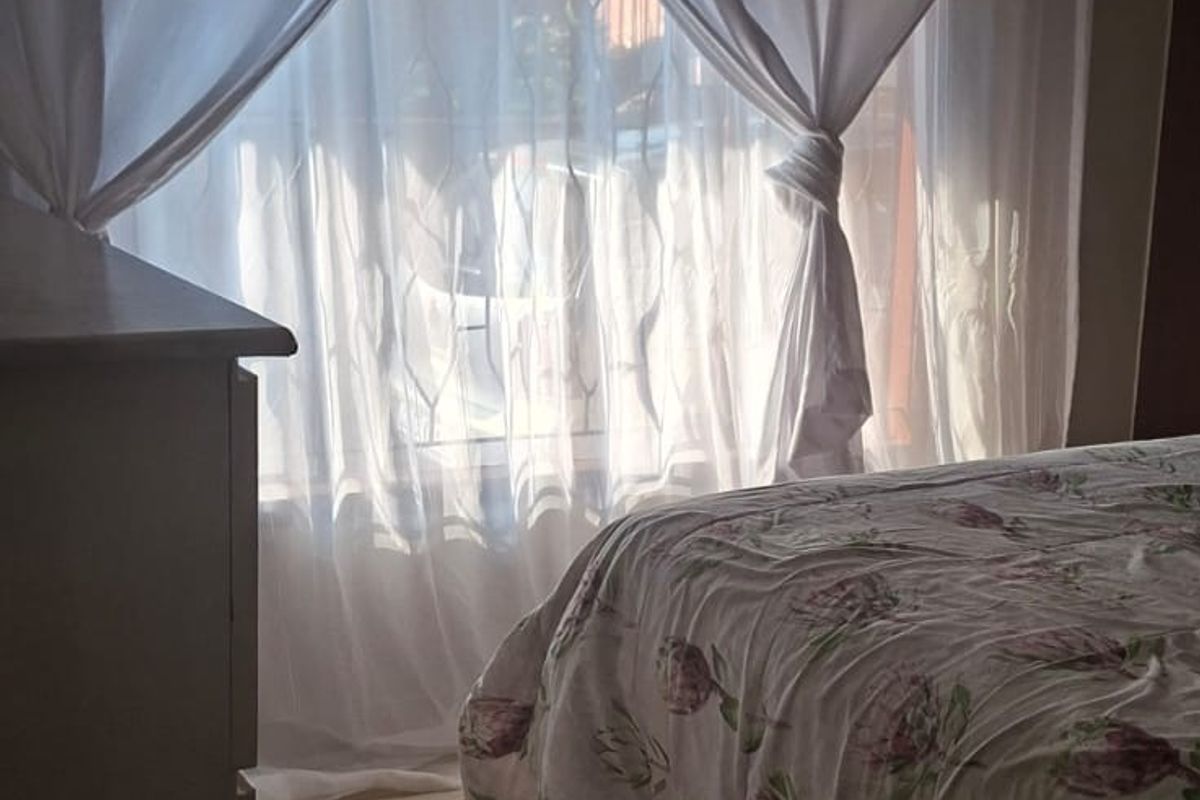 A bedroom featuring tiled flooring and a panelled ceiling, with natural light filtering through window curtains.