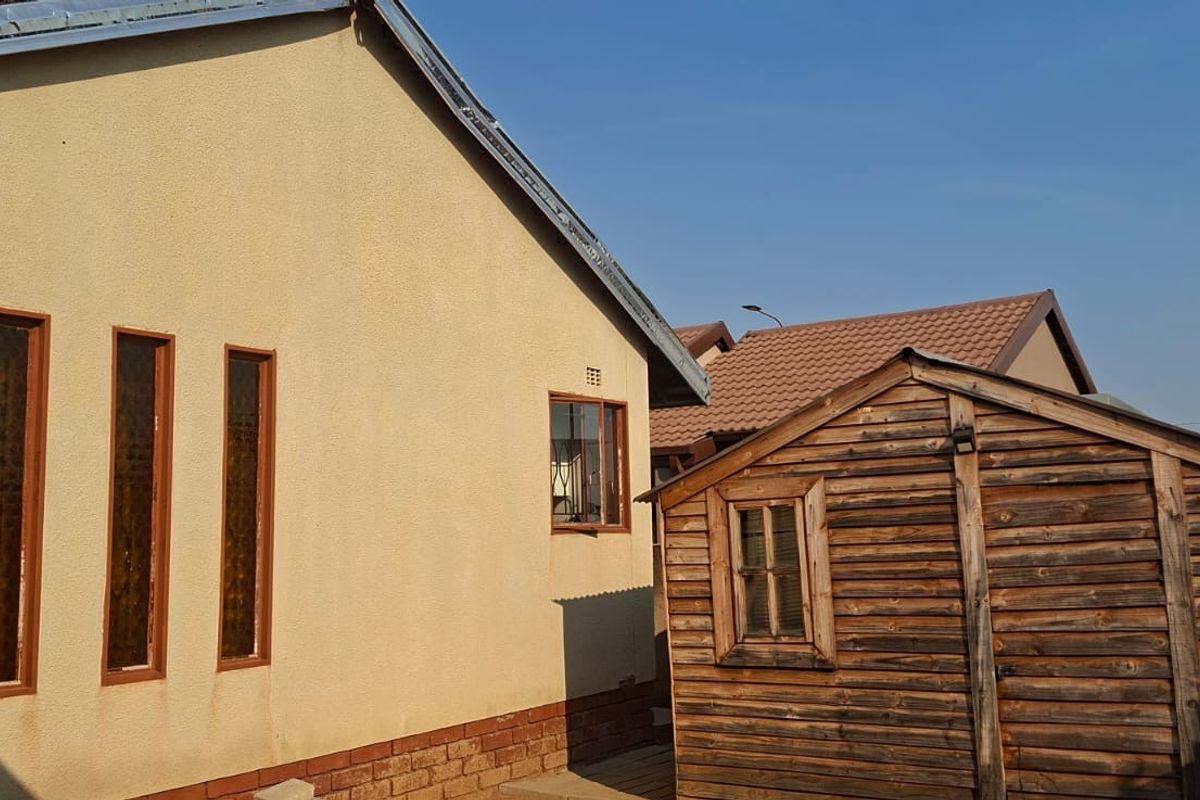 Rear exterior view of the property featuring a rendered wall with vertical windows and a detached timber storage shed.