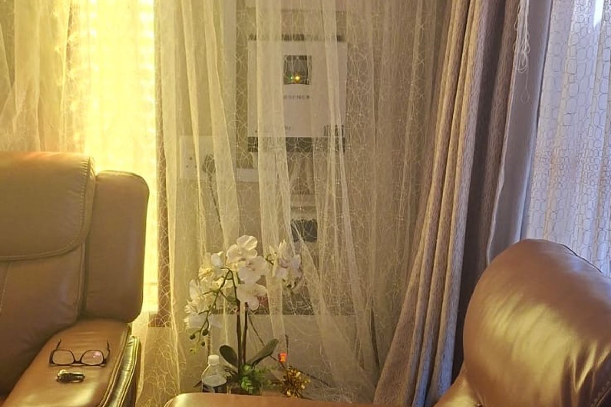 A living room area featuring a wall-mounted solar inverter and battery storage system, partially obscured by sheer curtains.