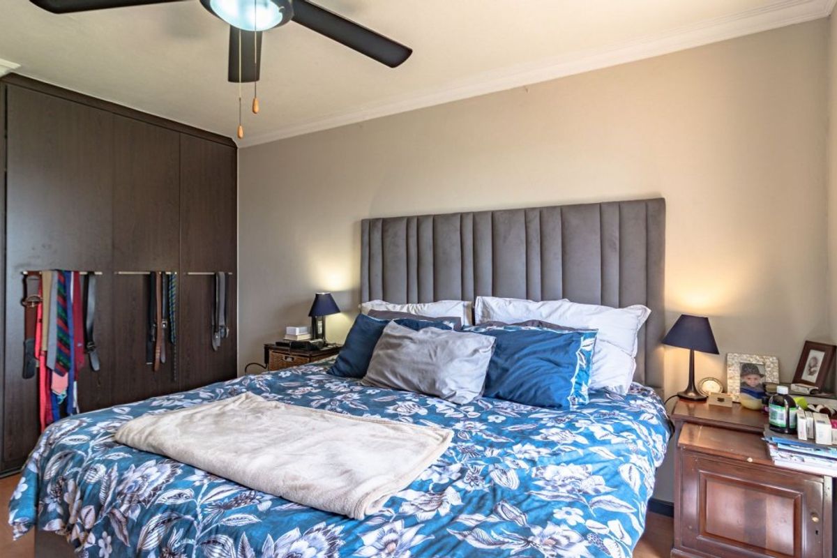 A well-maintained bedroom featuring dark wood built-in cupboards, a ceiling fan, and laminate flooring, providing a functional and comfortable living space.