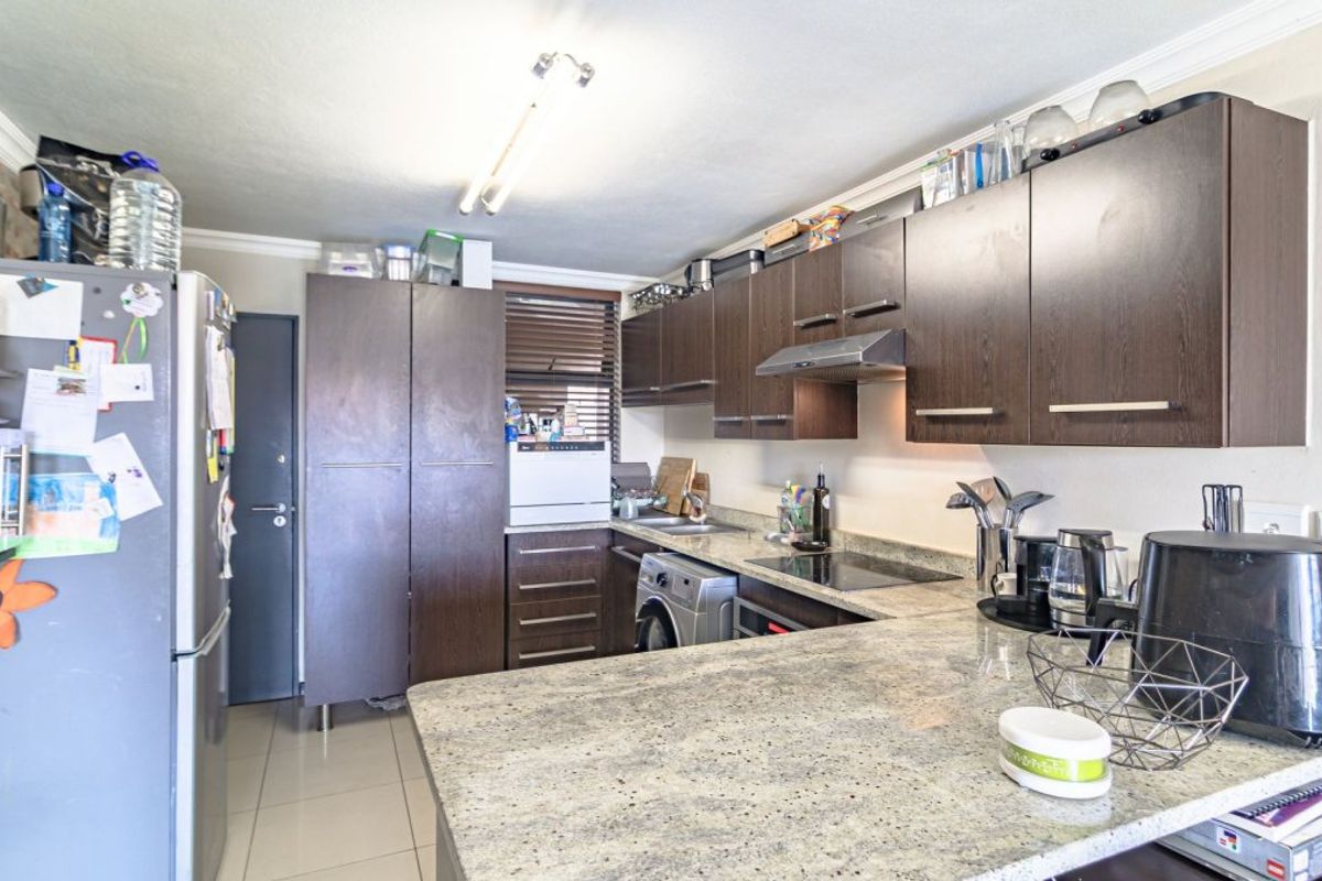 A functional kitchen featuring dark wood cabinetry, granite countertops, an electric hob, and an integrated extractor fan with tiled flooring.