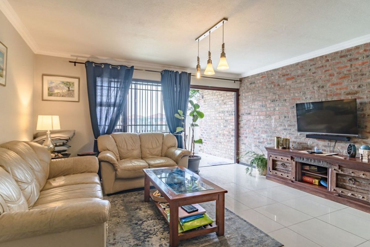 A spacious living room featuring an exposed brick wall, tiled flooring, and a sliding glass door providing access to the outdoor area.
