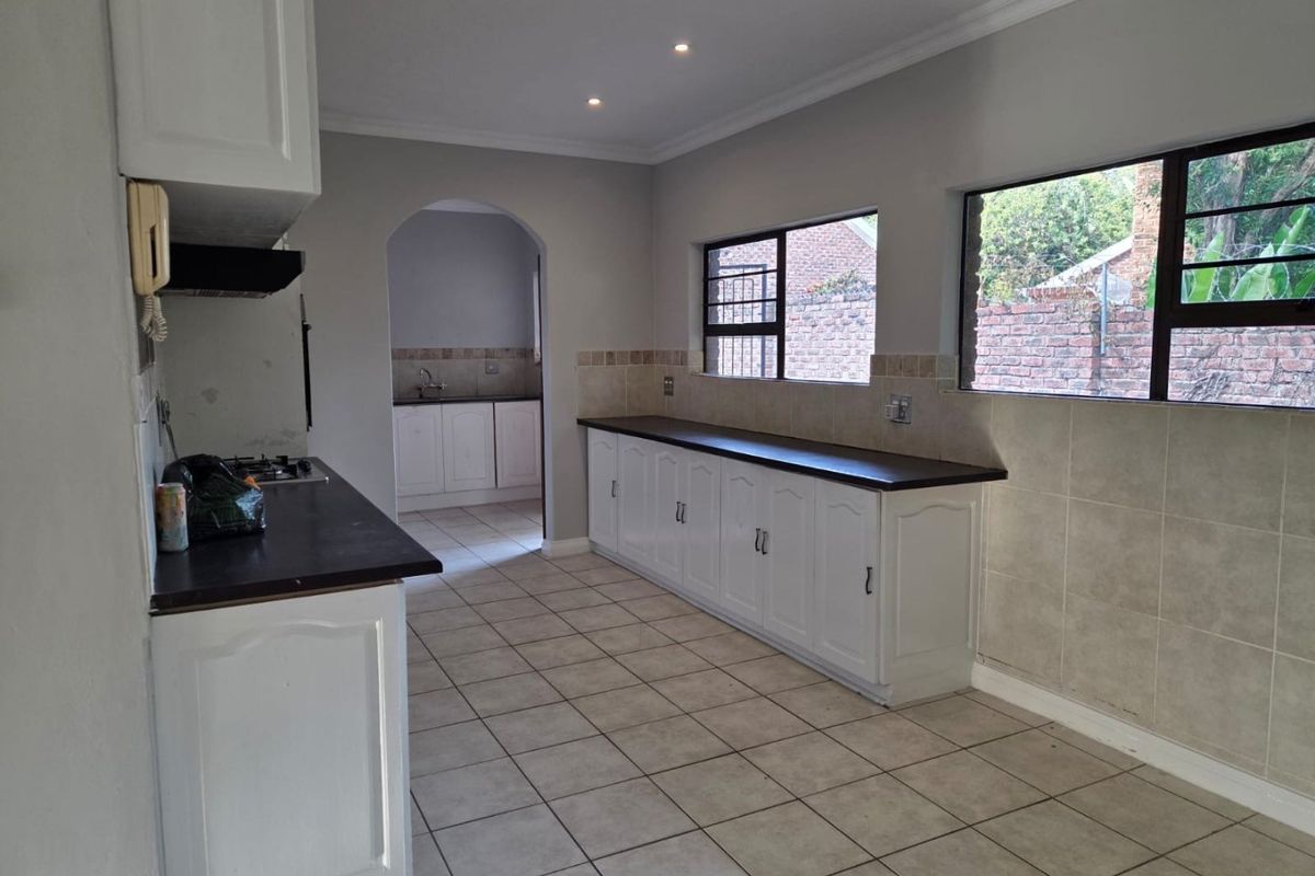 Spacious kitchen featuring white built-in cabinetry, dark laminate countertops, gas hob, extractor fan, and tiled flooring, with an adjoining scullery area.