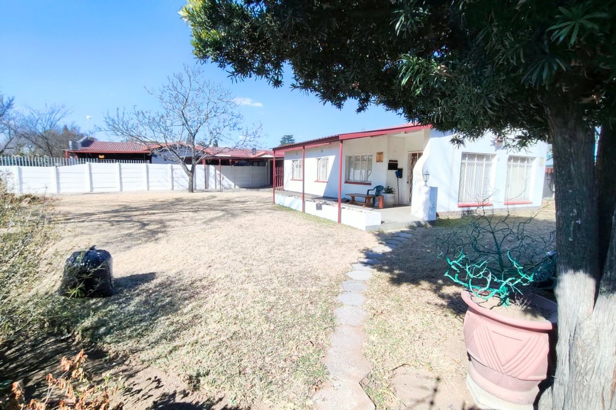 Rear view of the property featuring a covered patio, a large garden area, and a secure precast concrete boundary wall.