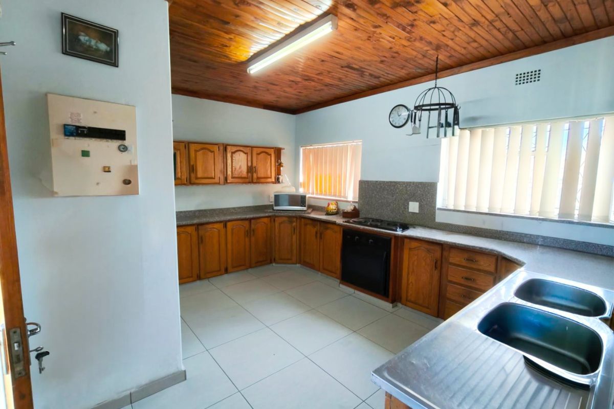 A functional kitchen featuring wooden cabinetry, stone countertops, built-in oven and hob, double stainless steel sink, and a distinctive timber tongue and groove ceiling.