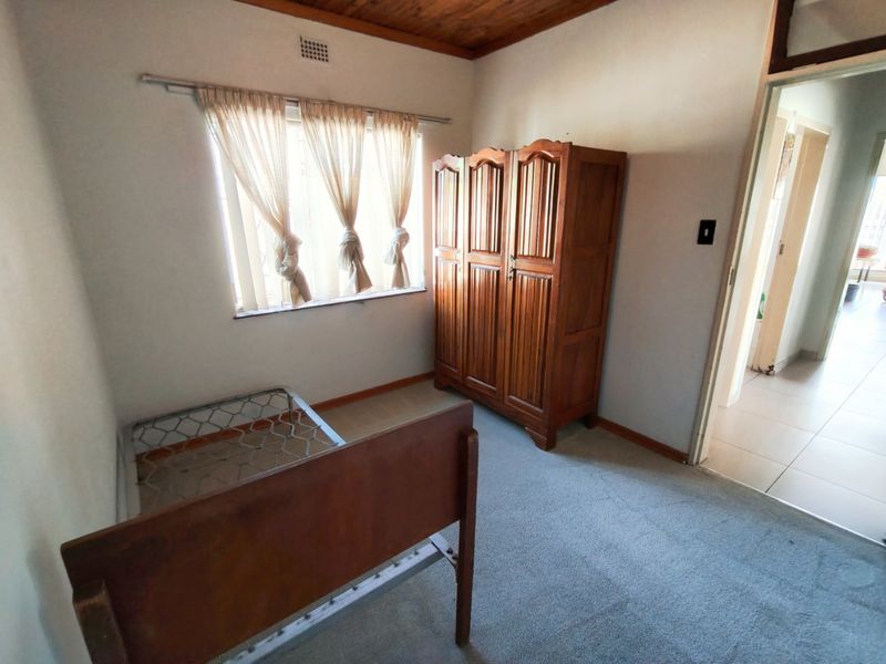 A bedroom featuring timber ceiling panels, carpeted flooring, and a window with security bars, offering a functional space in need of cosmetic updates.
