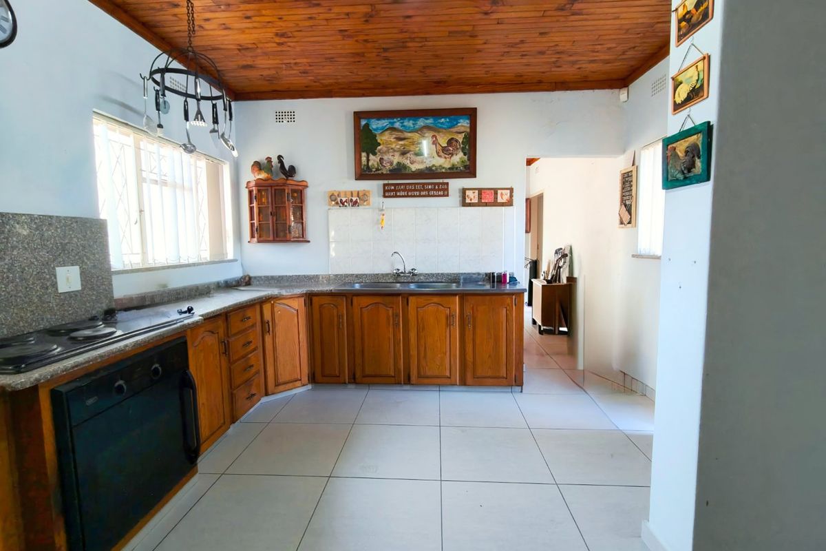 A functional kitchen featuring wooden cabinetry, granite countertops, built-in oven, hob, and a timber ceiling, offering a traditional aesthetic with potential for modernization.