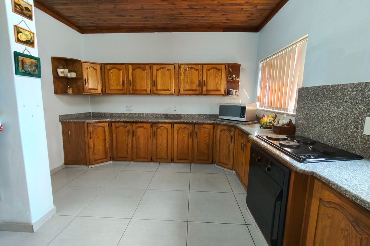 A functional kitchen featuring wooden cabinetry, granite countertops, a built-in oven, electric hob, and a distinctive timber ceiling with tiled flooring.
