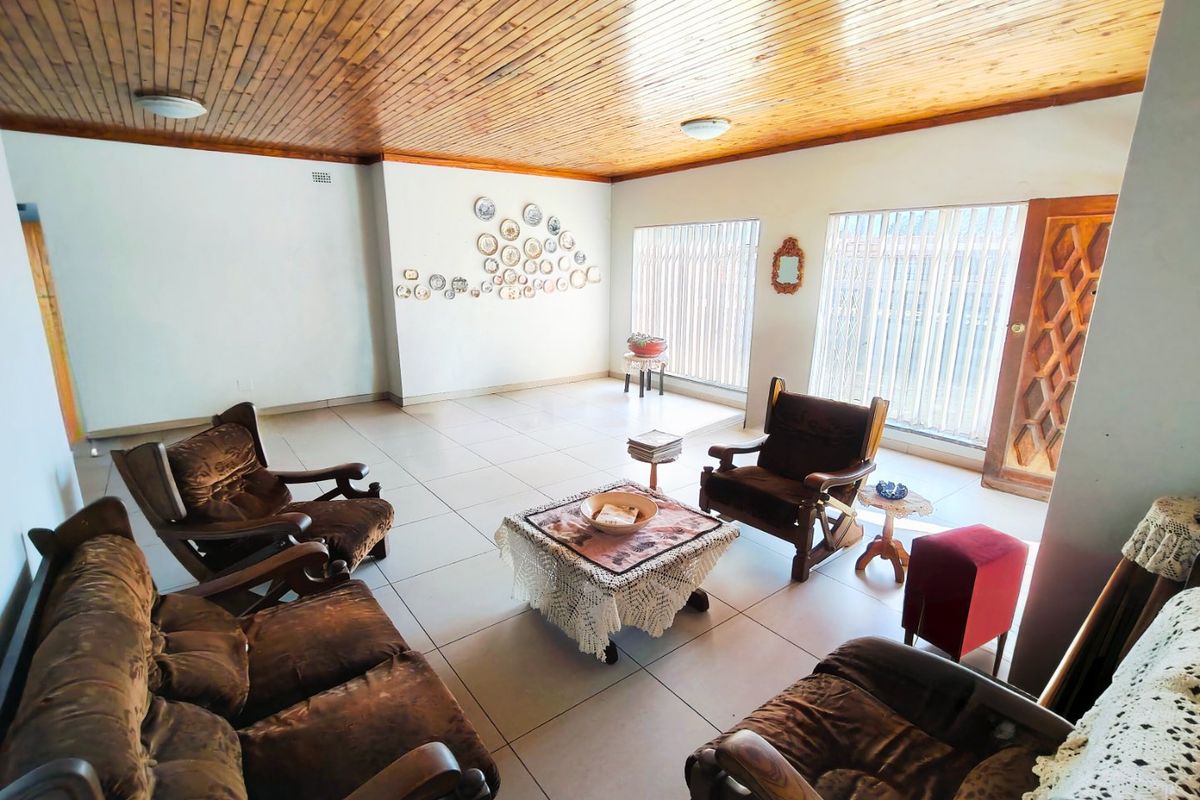 Spacious living room featuring a warm timber tongue and groove ceiling, neutral tiled flooring, and large windows with vertical blinds.