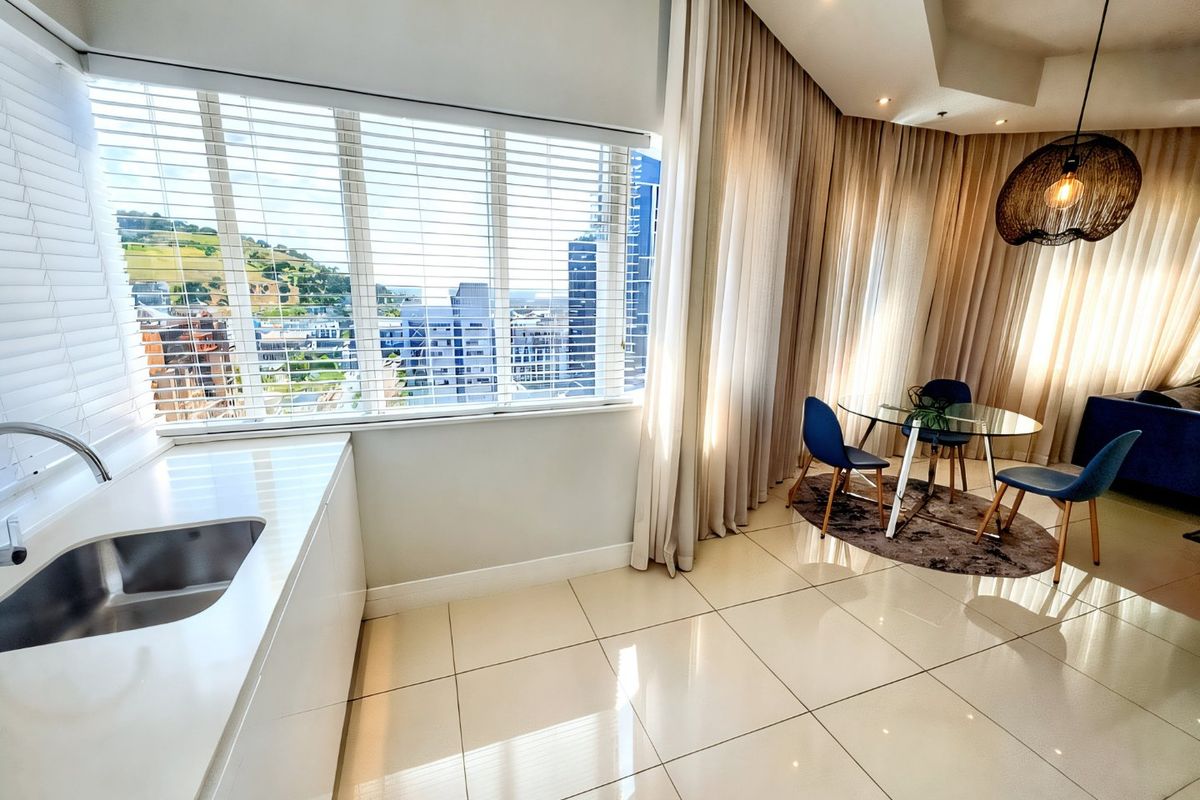 Modern open-plan living area featuring sleek tiled flooring, a compact kitchenette with stainless steel sink, and expansive windows offering urban views.