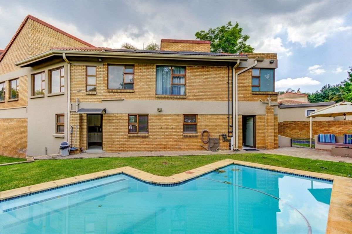 Rear exterior view of the house featuring a swimming pool, paved patio area, and brick facade with established garden surroundings.