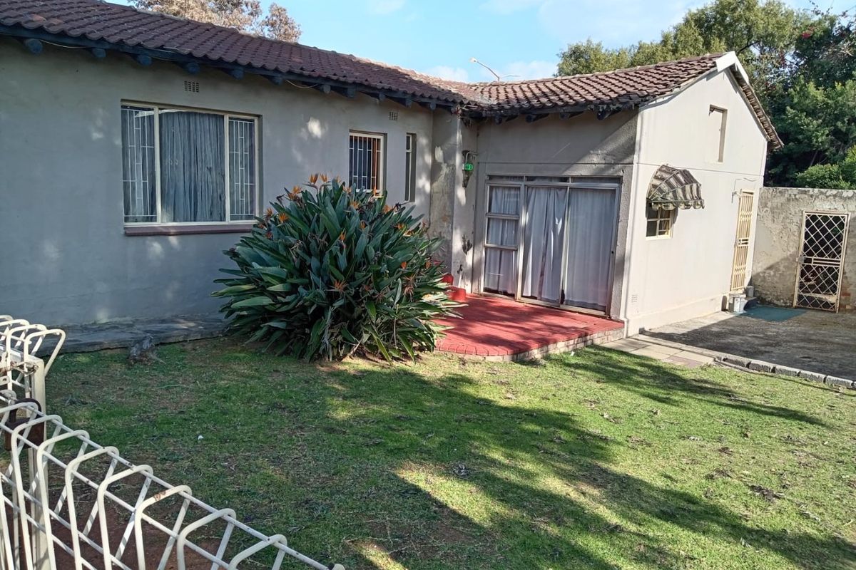 Rear view of the property featuring a tiled roof, sliding glass doors leading to a patio, and a private garden area with security fencing.