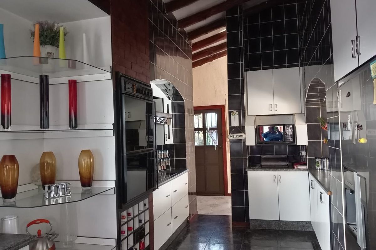 A functional kitchen featuring built-in appliances, dark tiled walls, granite countertops, and exposed timber ceiling beams.