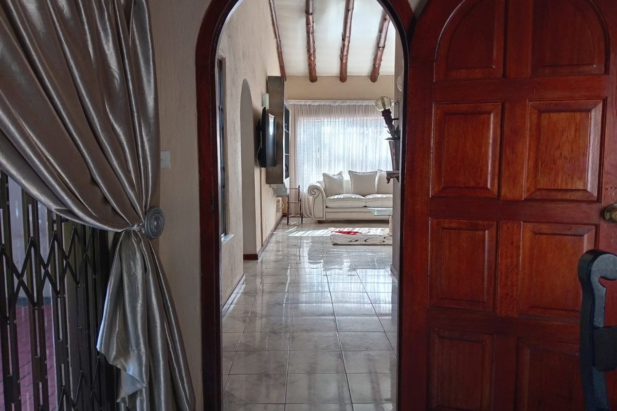 View through an arched doorway into a living area featuring tiled floors and exposed timber ceiling beams.
