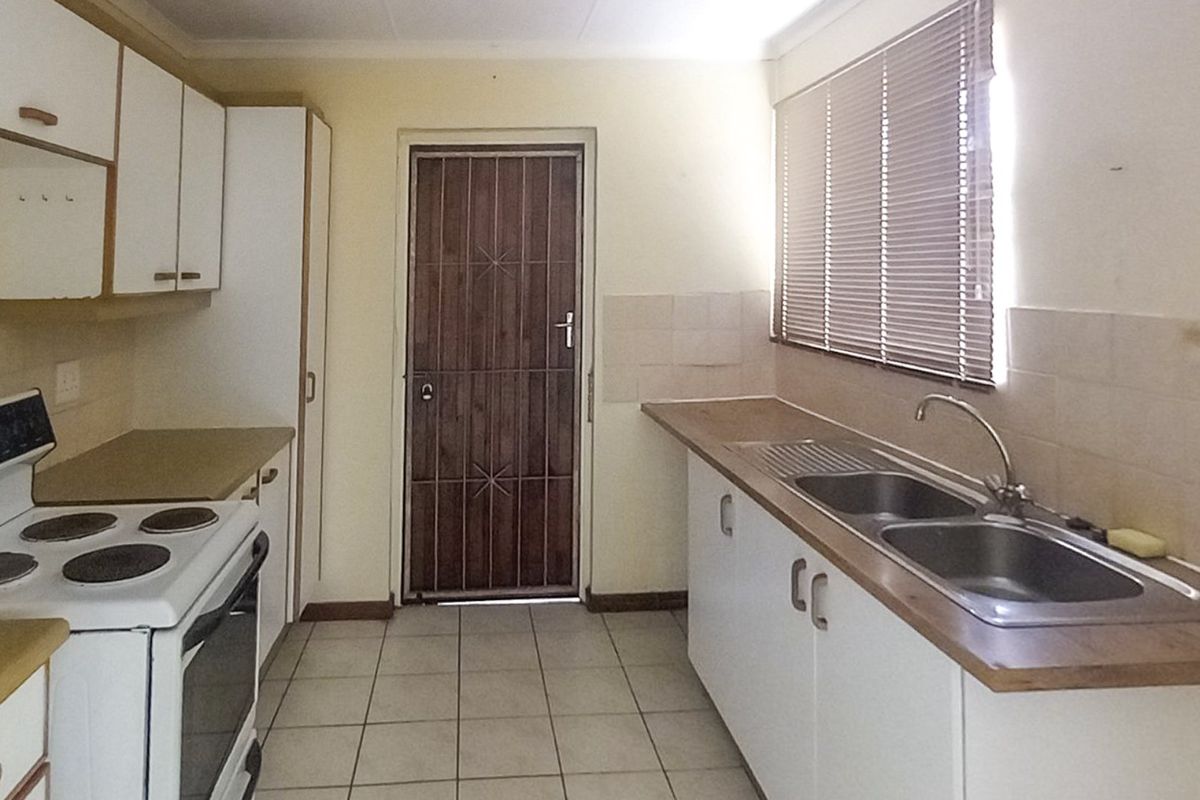 A functional kitchen featuring built-in cabinetry, laminate countertops, a double bowl sink, and an electric stove, with tiled flooring and a rear security door.