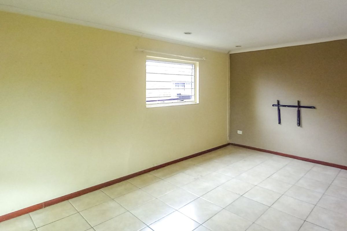An empty living room featuring tiled flooring, recessed lighting, and security bars on the window, offering a blank canvas for interior design.
