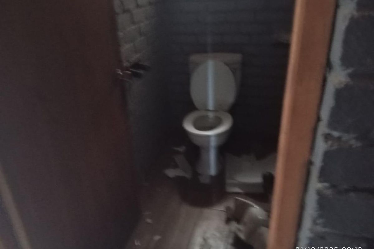 A small, unfinished industrial-style bathroom featuring exposed brick walls and a standard toilet fixture, requiring significant renovation and cleaning.