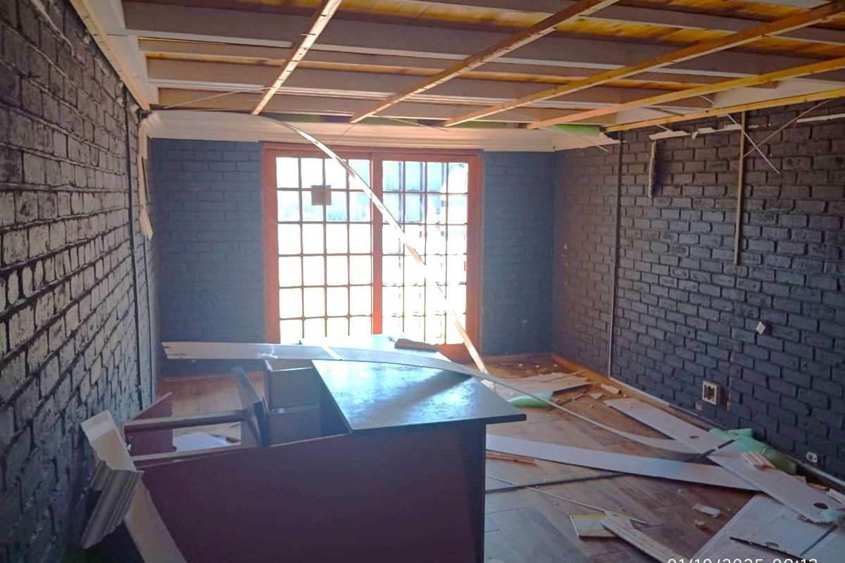 An industrial-style room under renovation featuring exposed brick walls, timber ceiling framing, and french doors, currently in a state of disrepair.