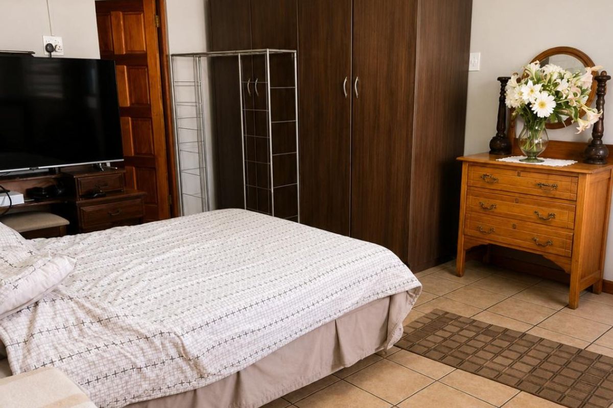 A functional bedroom featuring tiled flooring, a built-in wardrobe, and neutral wall finishes, providing a practical and comfortable living space.