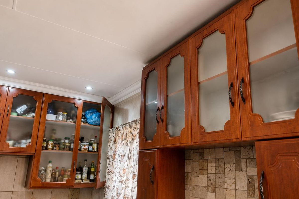 A kitchen area featuring traditional wooden cabinetry with glass-fronted doors and a decorative tiled backsplash.